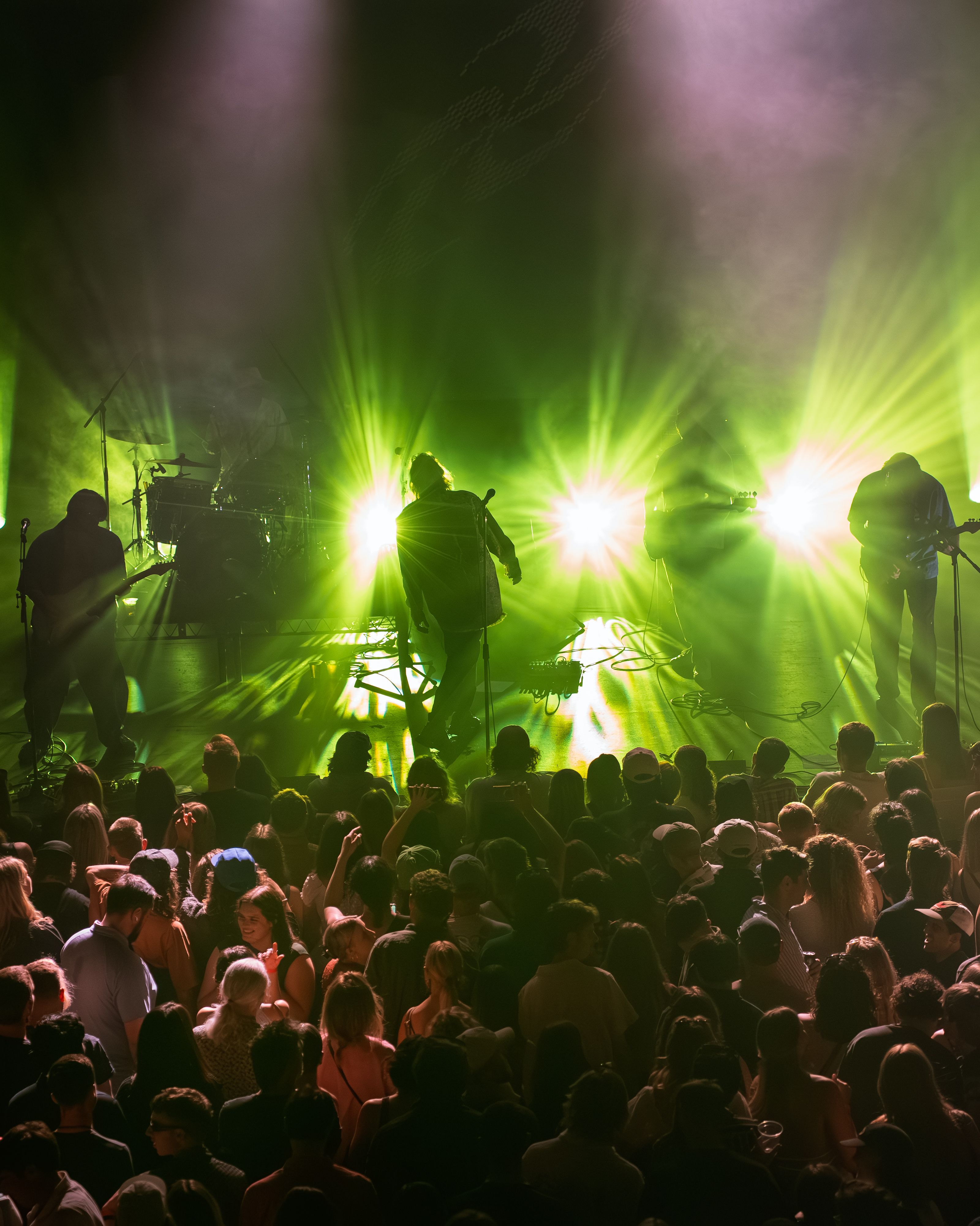 Bright green lights flash from the back of the stage, lighting up several silhouettes of people